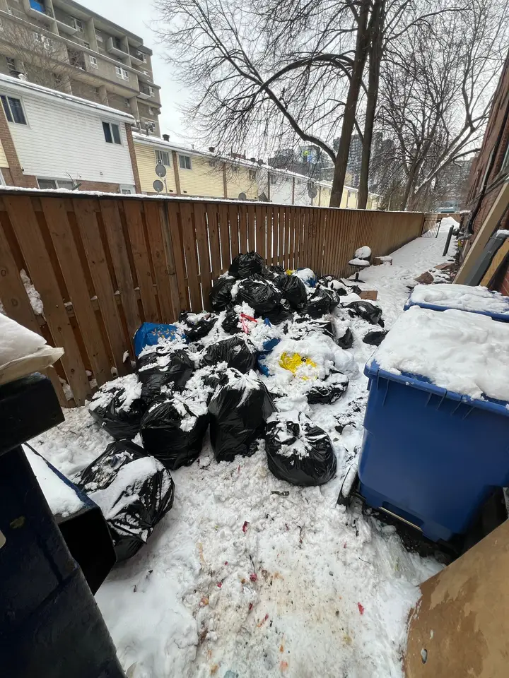 A large pile of garbage bags in the snow beside recycling bins