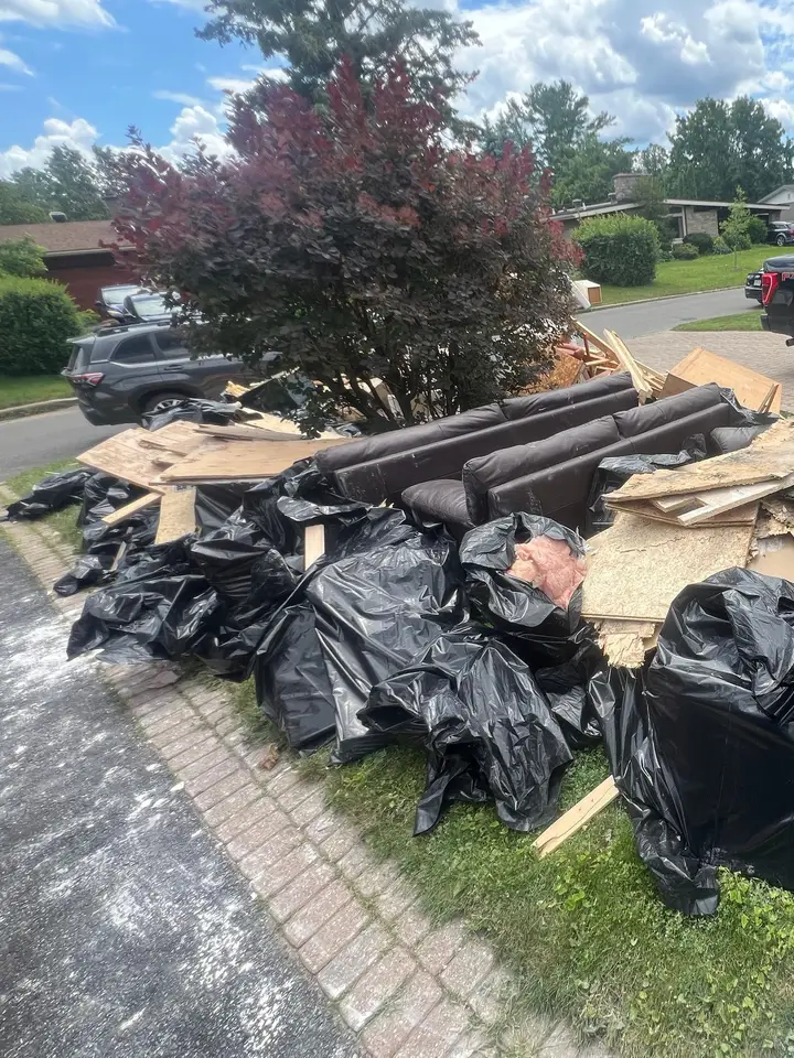 Bags of debris, old sofas and boards stacked beside a driveway